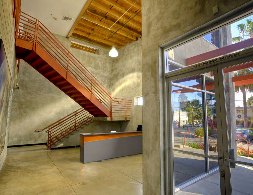 Two-story lobby with exposed orange-red steel stair and concrete walls
