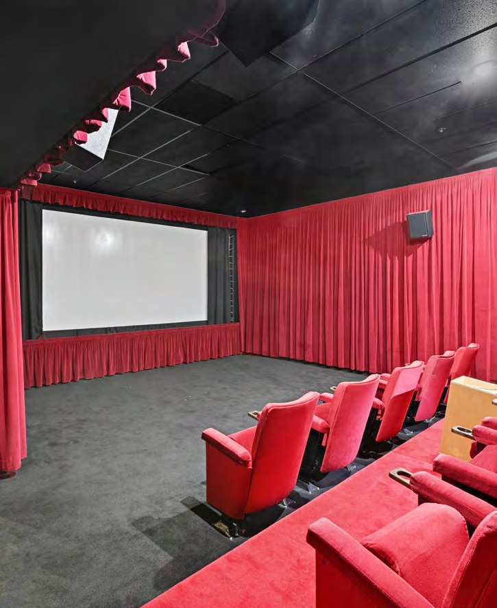 Screening room and theater with tiered red seating and a projection screen
